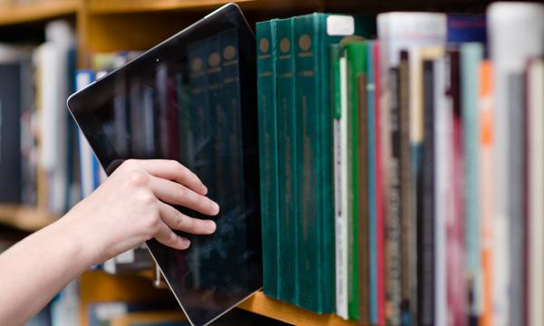 A hand reaching an ebook reader down from a bookshelf